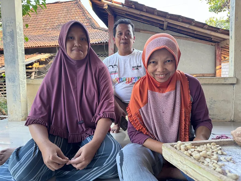 Producers shelling cashew nuts by hand beside a tray of kernels